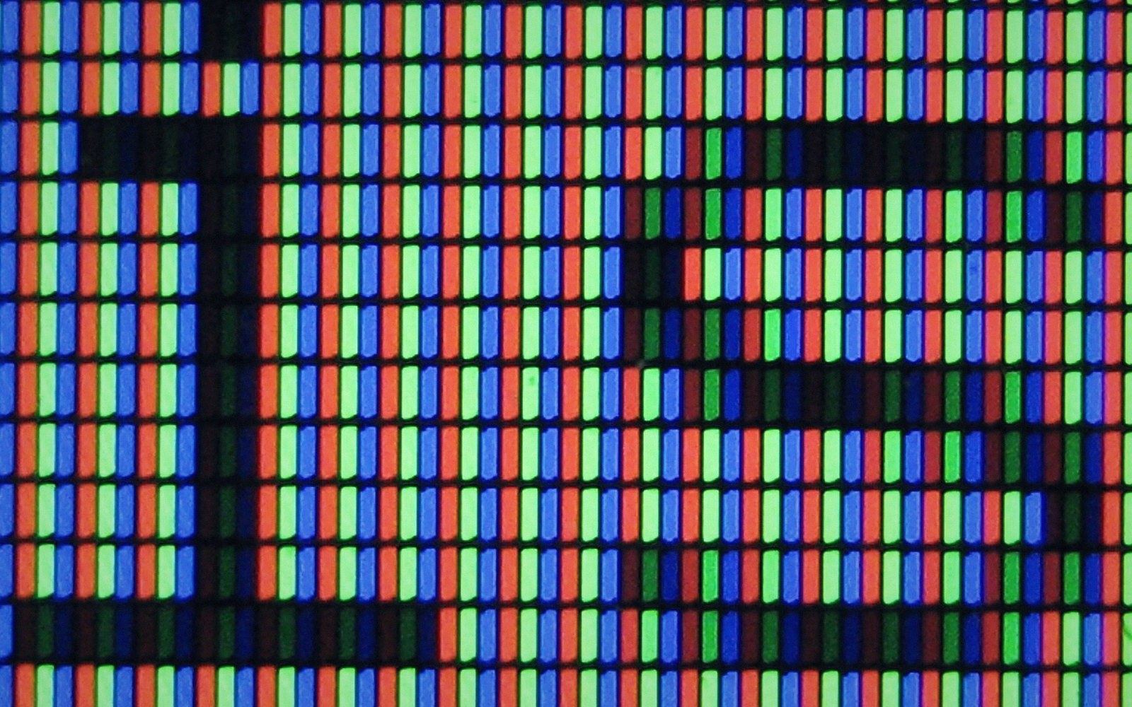 RGB subpixel triad array photographed at extreme macro, individual emitters clearly resolved against a dark panel substrate